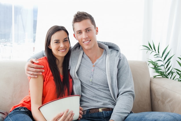 Una pareja sonriente sentada en el sofá mira a la cámara