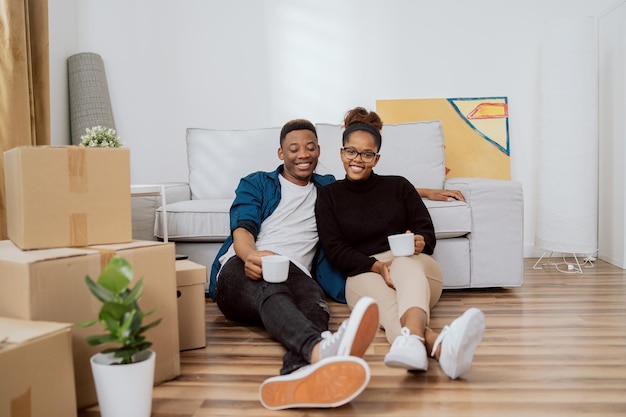 Una pareja sonriente sentada en el suelo relajándose después de mudarse