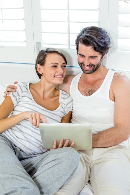 Pareja sonriente con tableta digital en cama