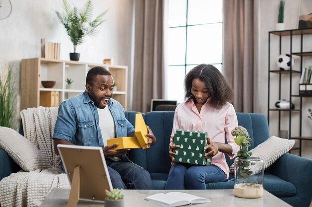 Pareja sorprendida abriendo cajas de regalo mientras se sienta en el sofá