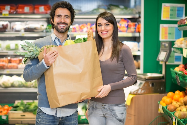 Pareja sosteniendo una bolsa llena de comida en el supermercado