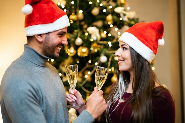 Pareja sosteniendo copas con champán celebrando las vacaciones de invierno de Navidad en casa juntos desean suerte y alegría Concepto de celebración