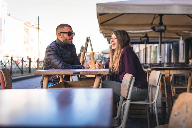 Pareja sosteniendo copas de vino en la mesa hablando mientras están sentados en una cafetería al aire libre