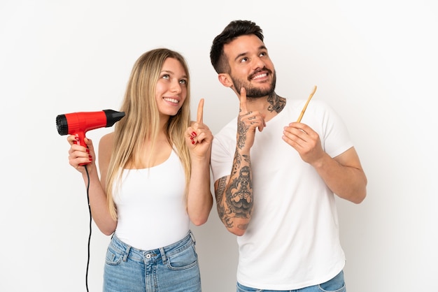 Pareja sosteniendo un secador de pelo y cepillarse los dientes sobre fondo blanco aislado apuntando con el dedo índice una gran idea