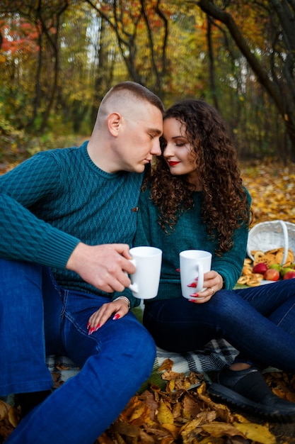 Pareja en suéteres bebe té en el bosque de otoño