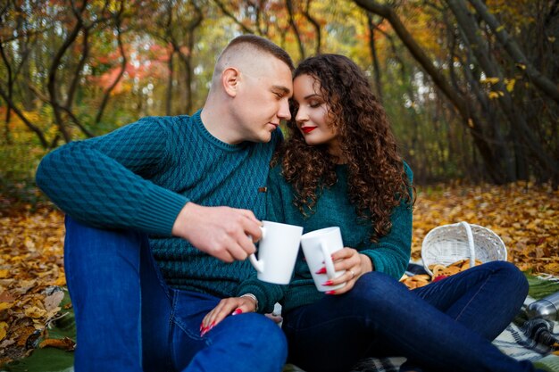 Pareja en suéteres bebe té en el bosque de otoño