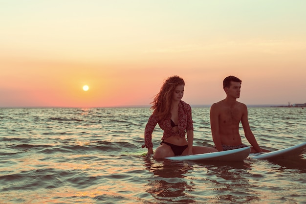 Pareja de surf apoyándose en tablas de surf en el mar