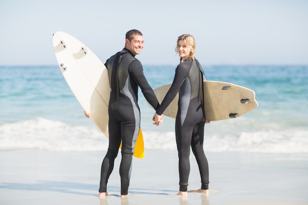 Pareja con tabla de surf mano en la playa