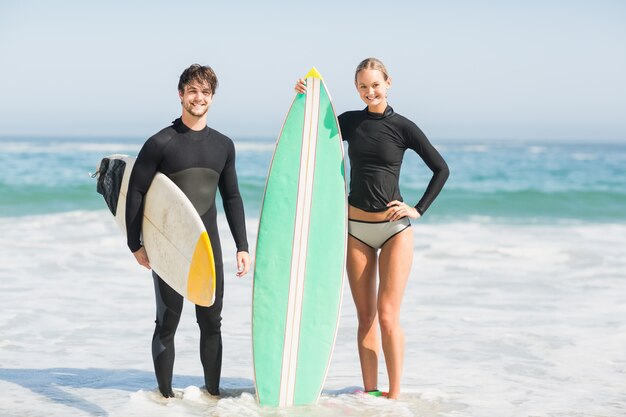 Pareja con tabla de surf de pie en la playa