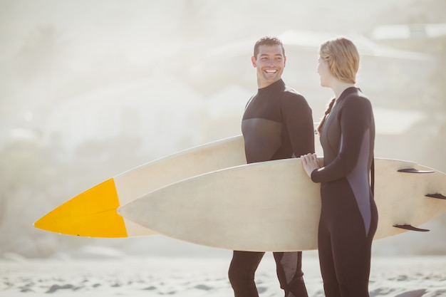 Pareja con tabla de surf de pie en la playa