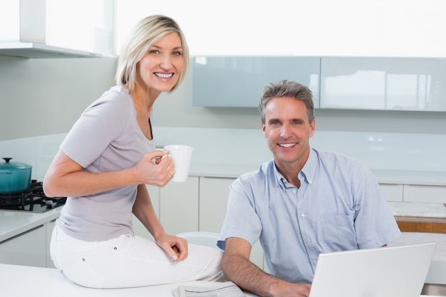 Pareja con taza de café y portátil en la cocina