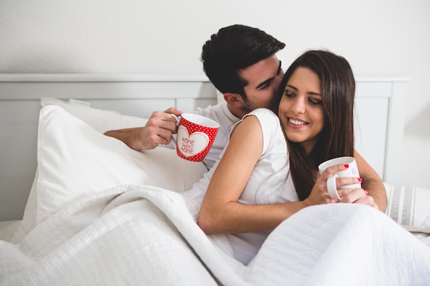 Pareja con tazas de café en la cama