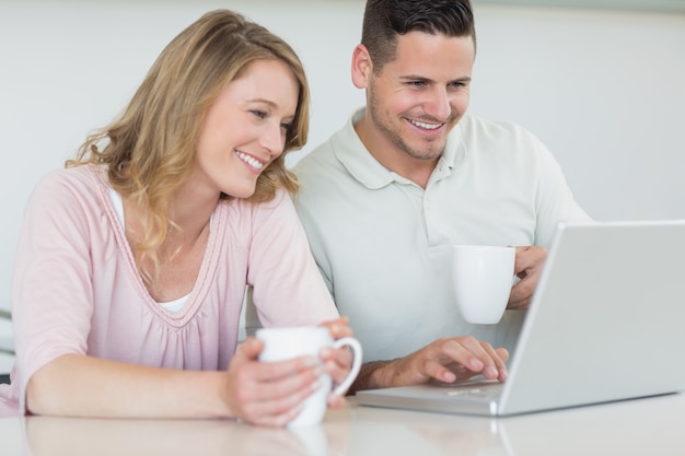 Pareja con tazas de café usando la computadora portátil en la mesa