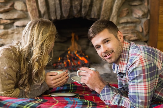 Pareja con tazas de té frente a la chimenea encendida