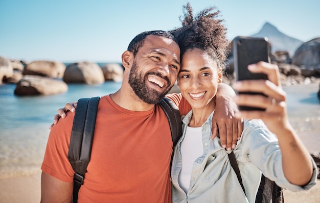 Pareja teléfono selfie y aventura de viaje en la playa juntos para vacaciones en las redes sociales y verano en la naturaleza Hombre mujer feliz y abrazo para fotografía de teléfono móvil en el mar del océano para la felicidad