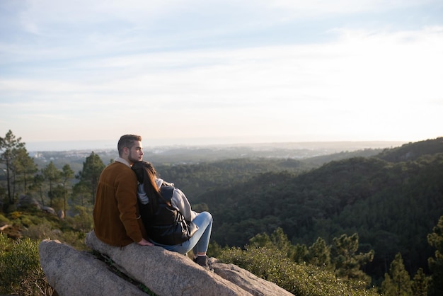 Pareja tierna descansando después de caminar en otoño. Hombre y mujer con ropa informal con munición de senderismo sentados en la cima, apoyados en el hombro. Naturaleza, actividad, concepto de hobby.