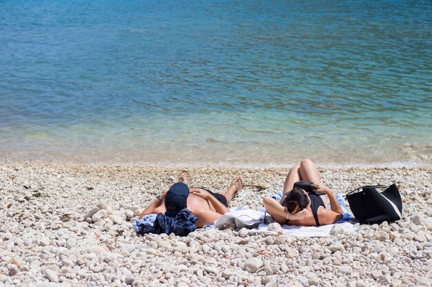 Una pareja toma el sol en una playa de guijarros cerca del agua