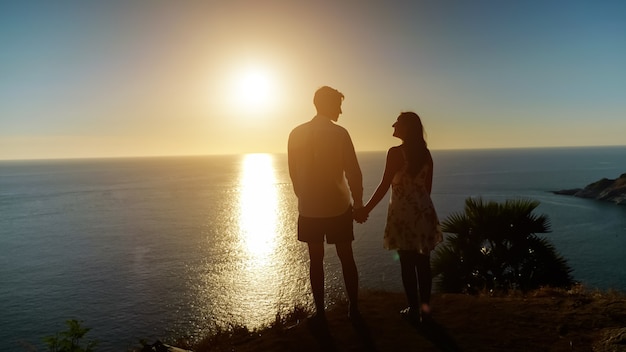 Pareja tomados de la mano va al borde del mirador al maravilloso atardecer reflejándose en el océano