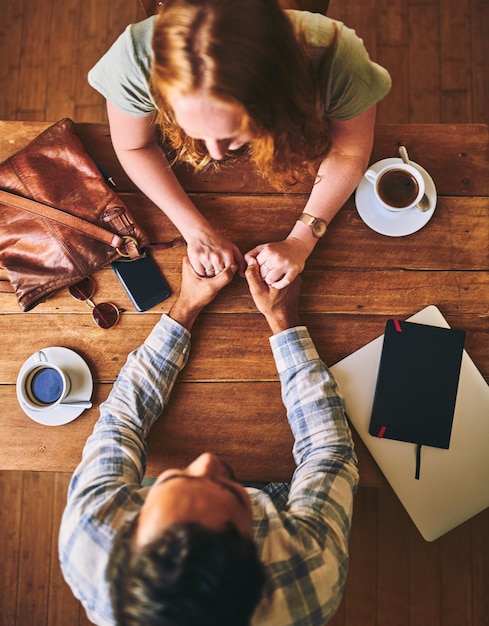 Pareja tomados de la mano amor y cita en la cafetería el día de San Valentín confianza y cuidado vista de la mesa de madera Personas en el café apoyan y respetan con compromiso y juntos en una relación