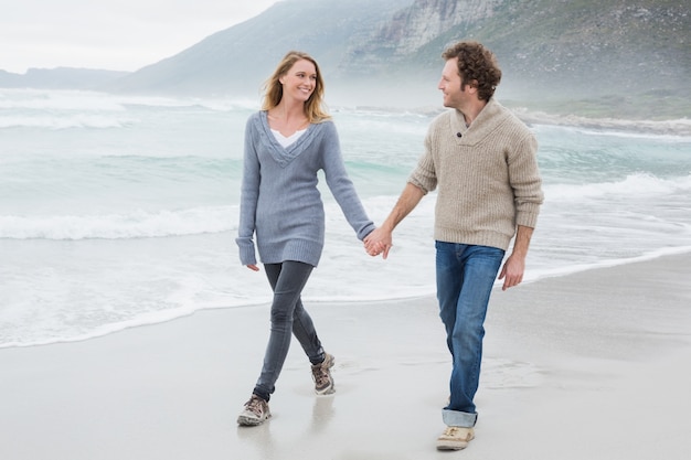 Pareja tomados de la mano y caminando en la playa