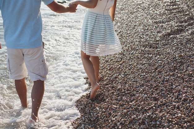 Pareja tomados de la mano caminando sobre los guijarros cerca del mar