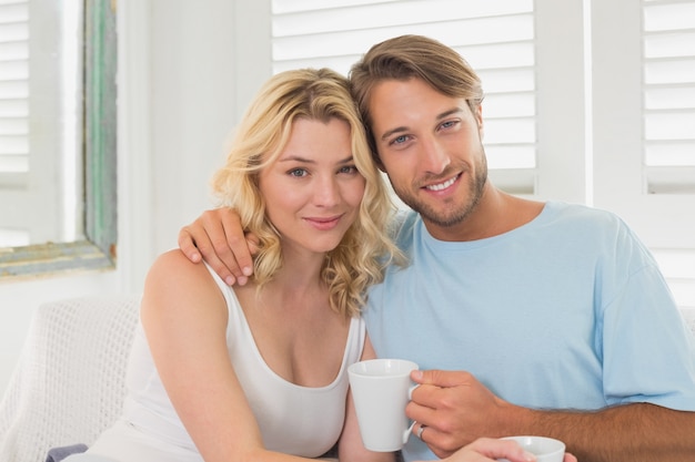 Pareja tomando un café en el sofá sonriendo a la cámara