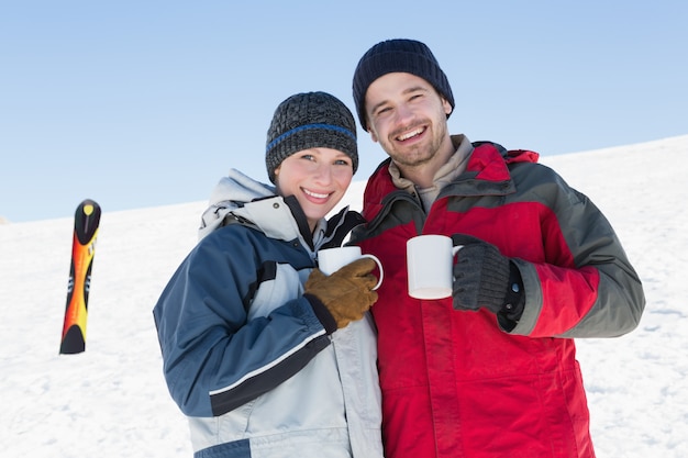 Pareja tomando un café con tabla de esquí en la nieve