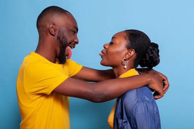 Una pareja tonta abrazándose y sacándose la lengua el uno al otro. Novia y novio jugando con un gesto tonto, expresando felicidad y romance cursi. Pareja positiva divirtiéndose.