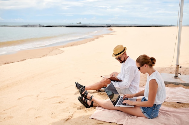 Pareja trabajando en línea en la playa