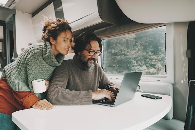 Pareja en el trabajo en la computadora portátil dentro de la autocaravana de viaje trabajo alternativo y estilo de vida Hombre y mujer usando juntos una computadora en una autocaravana de actividad de ocio interior Trabajo y libertad de vacaciones personas