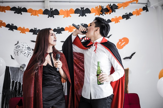 Foto pareja en traje de bruja y drácula celebran la fiesta de halloween y beben cerveza mientras cantan juntos.