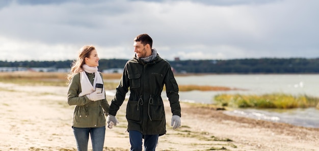 pareja con tumbler caminando a lo largo de la playa de otoño