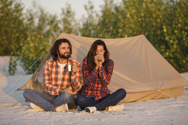 Pareja de turistas acampando cerca de la tienda al aire libre en la naturaleza