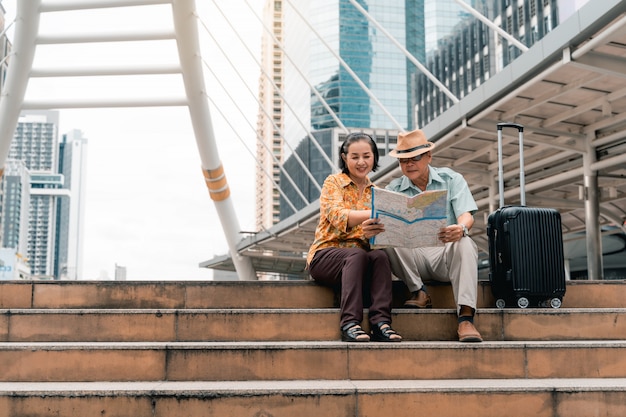 Una pareja de turistas asiáticos mayores que visitan la capital felices y se divierten y miran el mapa para encontrar lugares para visitar.