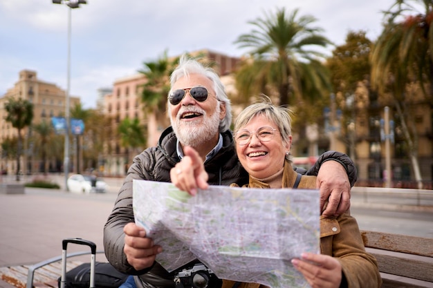 Foto una pareja de turistas caucásicos mayores sonriendo con un mapa de viaje en las manos mirando y señalando lugares