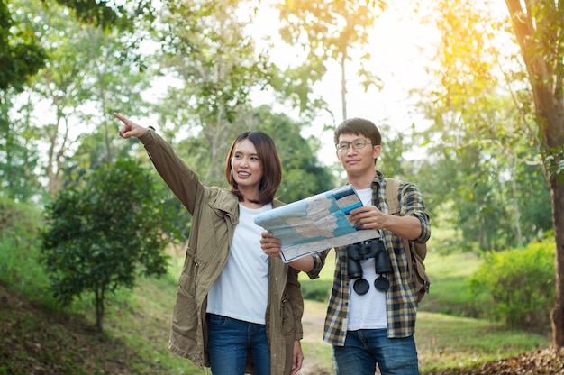 Pareja de turistas dirigiéndose al bosque con mapas en la mano en busca de su próximo destino