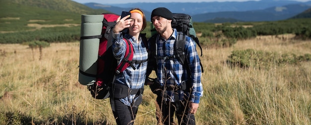 Una pareja de turistas enamorados, un hombre y una mujer parados en una llanura montañosa, se toman una selfie en un teléfono inteligente