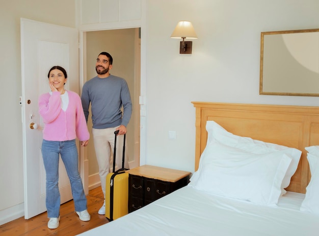 Pareja de turistas entrando en la habitación del hotel de pie con maleta en el interior