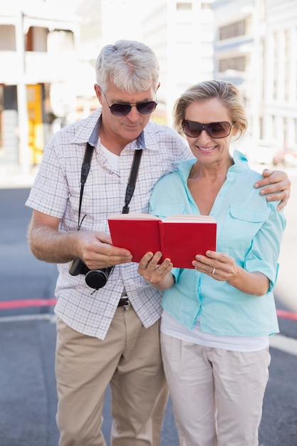 Pareja de turistas felices utilizando guía turística en la ciudad