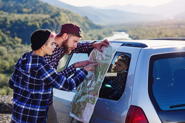 Pareja de turistas feliz con mapa de papel cerca del coche.