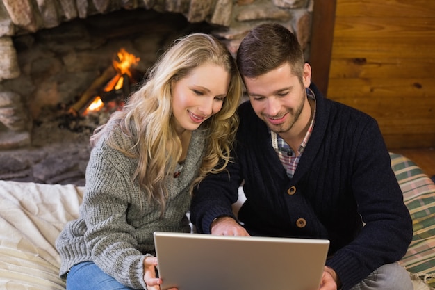 Pareja usando una computadora portátil en frente de la chimenea encendida