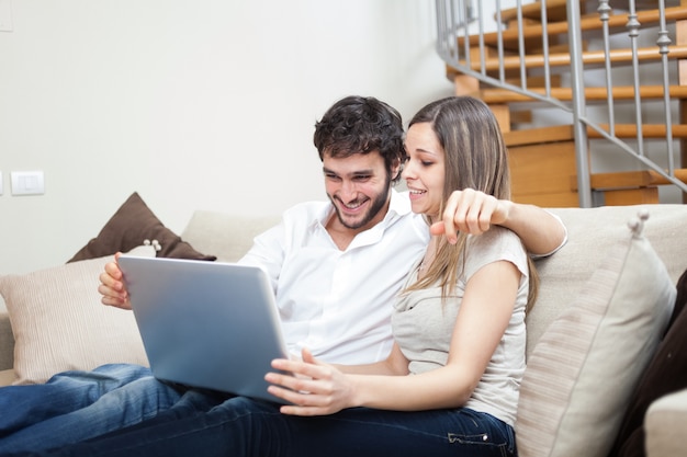 Pareja usando una computadora portátil mientras se relaja en el sofá