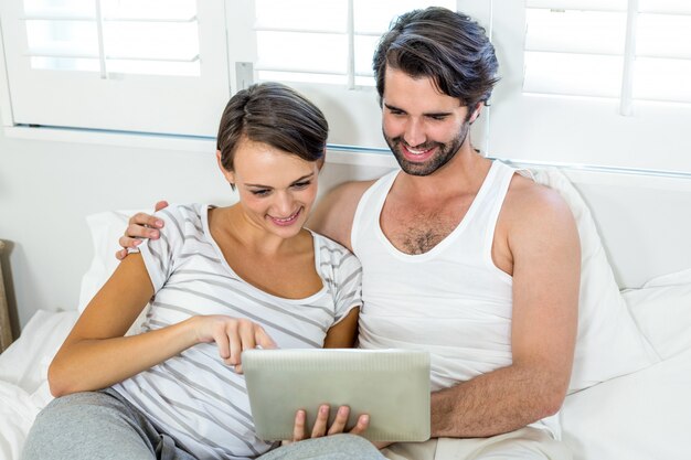 Pareja usando tableta digital mientras descansa en la cama