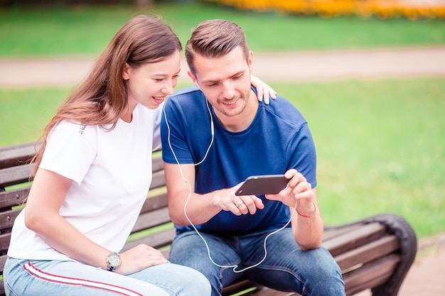 Pareja usando tableta y teléfono celular en parque público.