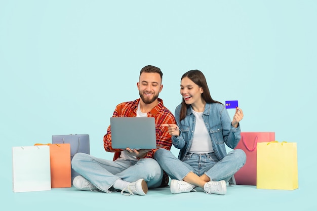 Foto pareja usando tarjeta de crédito y computadora portátil comprando sobre un fondo azul