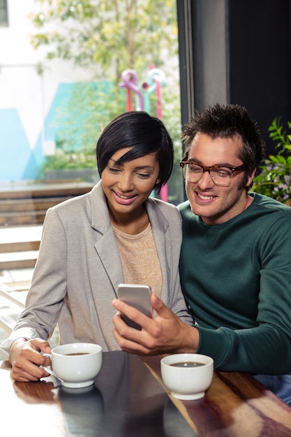 Pareja usando teléfono inteligente mientras bebe café