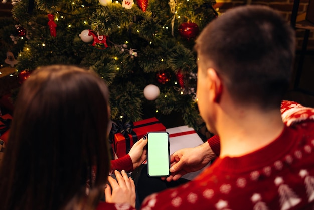 Pareja usando un teléfono inteligente para una videollamada navideña con una pantalla verde simulada festividad navideña