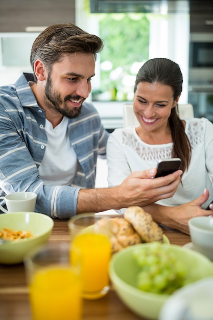 Pareja usando el teléfono móvil mientras desayuna