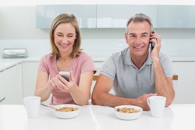 Pareja usando teléfonos celulares mientras desayuna en la cocina