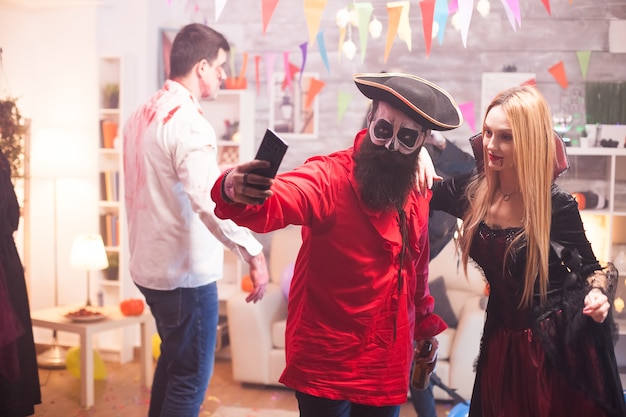 Pareja vestida como un pirata y un vampiro tomando un selfie en la fiesta de Halloween.